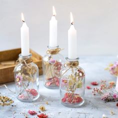 three glass bottles filled with flowers and candles