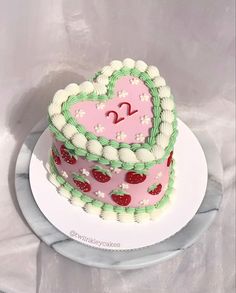 a heart shaped cake with white frosting and strawberries on the top is sitting on a plate