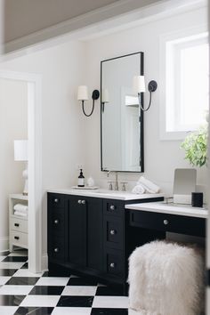 a bathroom with black and white checkered flooring, two vanity lights, an open laptop computer on the counter