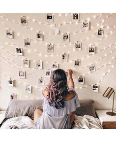 a woman sitting on top of a bed in front of a wall covered with pictures