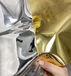 a person holding a piece of metal in front of a shiny gold wallpaper design