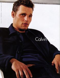 a man sitting on top of a white chair next to a wall wearing a blue shirt