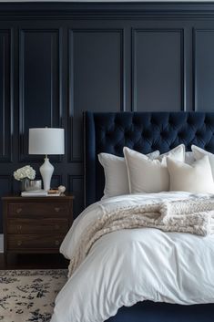 a bedroom with dark blue walls and white linens on the bed, along with an upholstered headboard