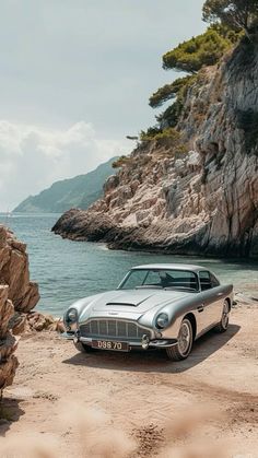 an old car is parked on the beach by the water's edge in front of some rocks