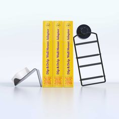 three books are sitting next to each other in front of a yellow book rack and two metal objects