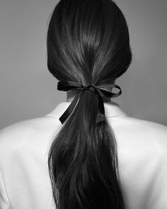 a woman with long black hair wearing a bow in her back's ponytail, looking to the side