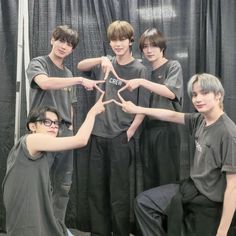 five young men standing in front of a black curtain making the shape of a star with their hands