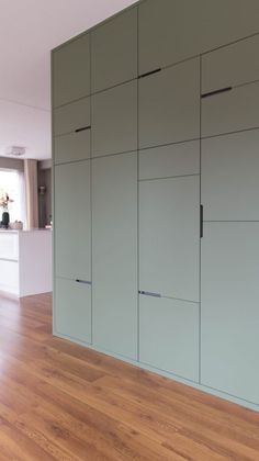 an empty room with wood flooring and green cupboards on the wall behind it