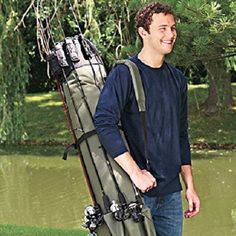 a man holding a golf bag in front of a pond with trees and water behind him