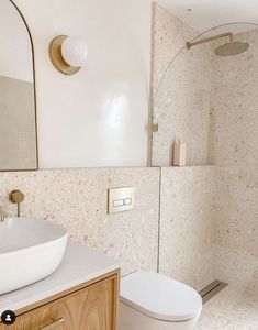 a white toilet sitting next to a sink in a bathroom under a shower head mounted on a wall