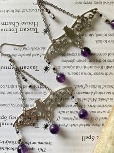 Cast bat charms drop from stainless steel chain with Czech glass beads, flashy faceted Moonstone, and deep dreamy Amethyst--a combination of stones which will keep you calm and collected amidst any chaos! Connecting to the divine energy of the moon, Moonstone enhances intuition and psychic energy. Working through the heart, third eye and crown chakras, it allows you to see past the obvious to deep and hidden truths. Just as the moon waxes and wanes, moonstone can help in processing changed and b Purple Pierced Metal Jewelry, Purple Metal Pierced Jewelry, Purple Jewelry With Dangling Charms For Gifts, Purple Crystal Metal Earrings For Gifts, Purple Metal Crystal Earrings As Gift, Purple Metal Crystal Earrings For Gift, Purple Metal Jewelry For Halloween, Handmade Mystical Crystal Earrings As Gift, Purple Metal Dangle Crystal Earrings