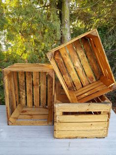 two wooden boxes sitting on top of a white table next to a tree and bushes