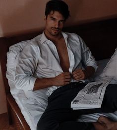 a man in white shirt and black pants sitting on a bed with his tie undone