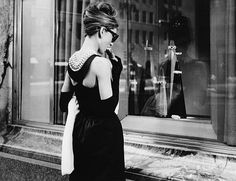 a woman walking down the street in front of a store window wearing a black dress