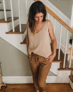 a woman standing in front of some stairs wearing brown pants and a tan tank top