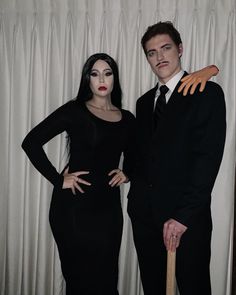 a man and woman dressed up in black posing for a photo with an orange bat