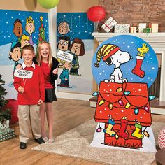 two children are standing in front of a christmas scene with snoopy on the chimney