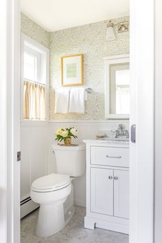 a white toilet sitting next to a sink in a bathroom under a window with yellow curtains