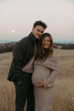 a pregnant couple posing for a photo in the middle of a wheat field at sunset