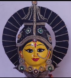 a yellow mask with jewels on it is hanging from the wall in front of a white wall