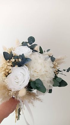 a bridal bouquet with white flowers and greenery is held by someone's hand