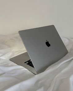 an apple laptop computer sitting on top of a white sheet covered bed with the cover pulled down