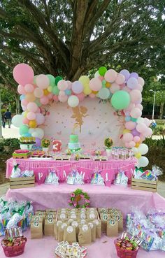 a pink table topped with lots of balloons and desserts next to a large tree