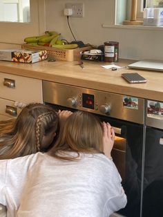 two girls looking into an oven with bananas on the counter