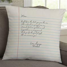 a pillow with writing on it sitting in front of a couch next to a window