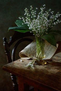 a vase filled with white flowers sitting on top of a wooden table next to an open book