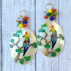 Compelling mother of pearl dangle earrings with a magnificent hand-painted tropical bird sitting on a branch design. A cluster of colorful beads gives a little soothing clatter sound against the mother of pearl. These artsy earrings have a 3.5-Inch drop and 1.75-Inch width, with gold-plated nickel-free lever back ear wires. Thanks for looking! Multicolor Bird Design Jewelry, Bohemian Mother Of Pearl Drop Earrings, Multicolor Bird Design Earrings For Gift, Multicolor Bird Design Earrings As A Gift, Multicolor Bird Design Earrings Gift, Gift Multicolor Bird Design Earrings, Artsy Earrings, Bird Sitting, Upcycled Art