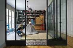 two people are looking through glass doors at a living room with bookshelves and furniture