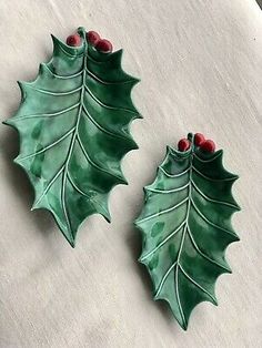 two green holly leaves with red berries are sitting next to each other on a table