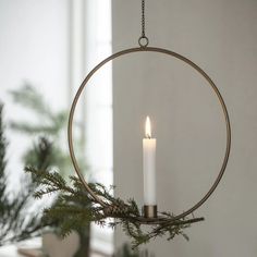 a candle that is inside of a circular metal ring hanging from a tree branch in front of a window