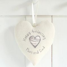 a white heart hanging on the side of a wall with an embroidered message that says happy anniversary dad and dog mum