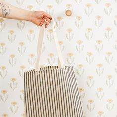 a person holding a striped bag in front of a wallpapered background with flowers