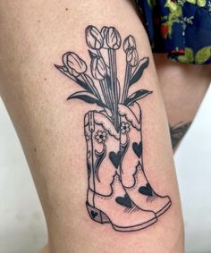 a woman's thigh with a boot and flowers tattoo on her leg, next to a flower pot