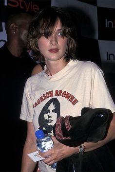 a woman holding a water bottle in her right hand and wearing a t - shirt with the rolling stones on it