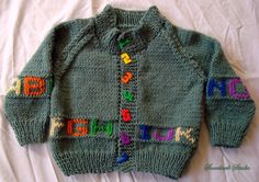 a child's green sweater with colorful letters on the front and back, sitting on a white sheet