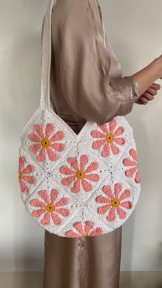 a woman is holding a crocheted bag with pink flowers on the front and sides