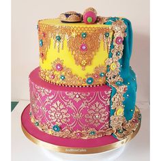 a three tiered cake decorated with gold, blue and pink