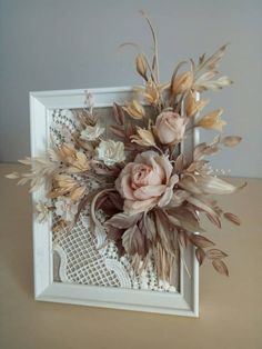 an arrangement of flowers in a white frame on a table