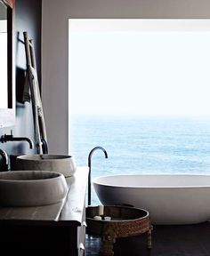 a bath tub sitting next to a window in a bathroom near the ocean with large windows