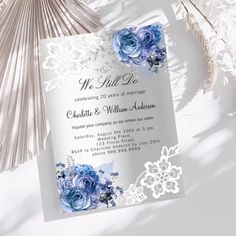 a wedding card with blue flowers and lace on the front, sitting next to a fan