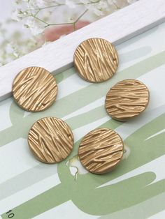 four gold buttons sitting on top of a wooden table next to white and green flowers