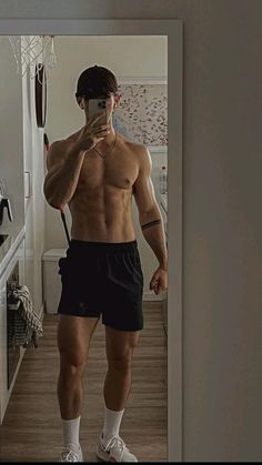 a shirtless man taking a selfie in the mirror with his cell phone while wearing shorts and socks