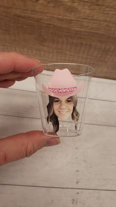 a person is holding a plastic cup with a photo on it and wearing a pink cowboy hat