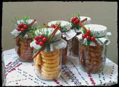 four jars filled with cookies on top of a table covered in red berries and cinnamon sticks