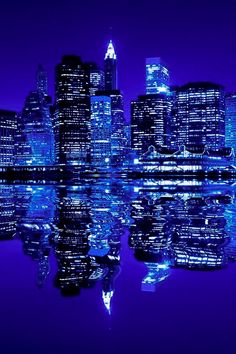 the city is lit up at night and reflecting in the water