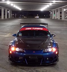 a blue sports car parked in a parking lot with its hood up and lights on